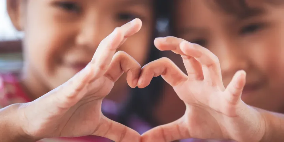 Two cute asian child girls making heart shape with hands together